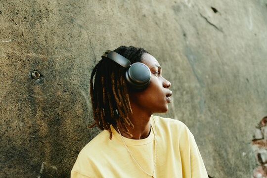 Young African American young adult with dreadlocks wearing headphones outdoors, looking away. Image represents youth culture and is ideal for audio brand marketing campaigns