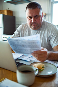 Concerned middle-aged man reviewing household bills at kitchen table