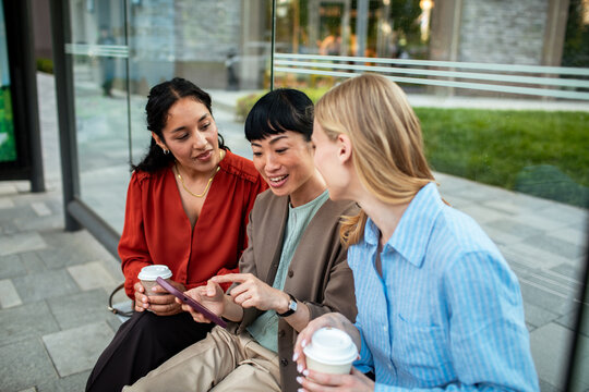 Three women collaborating with tablet at bus stop