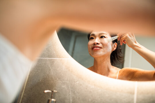 Smiling woman applying facial mask in bathroom mirror
