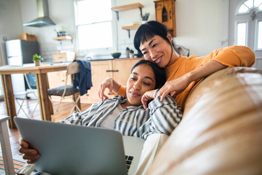 Two women relaxing on couch with laptop at home