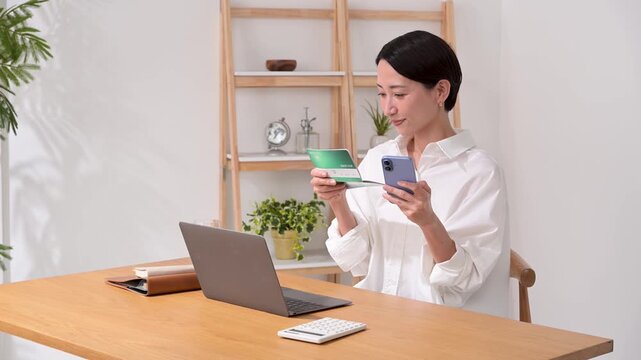 通帳を見ながらパソコン操作をする女性