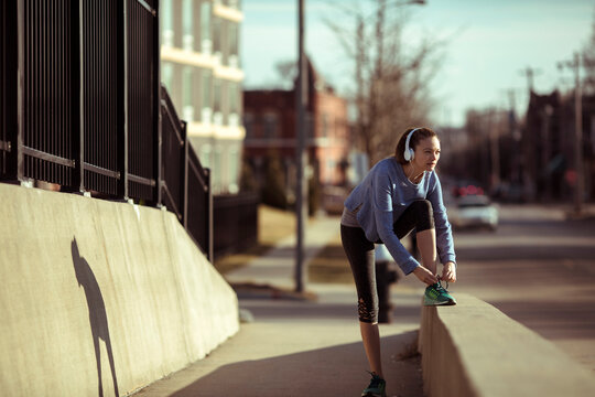 Young woman tying running shoes on urban sidewalk