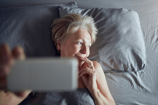Senior woman taking selfie in bed at home