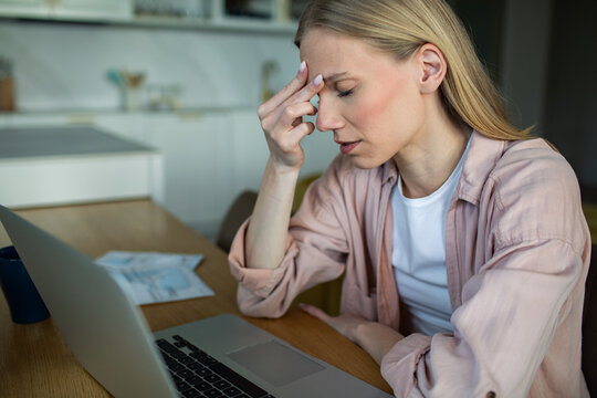 Stressed woman with headache working from home at kitchen table
