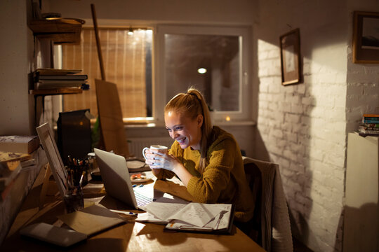 Smiling woman working at laptop in cozy home office at night