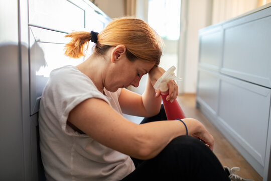 Tired woman resting on kitchen floor after cleaning