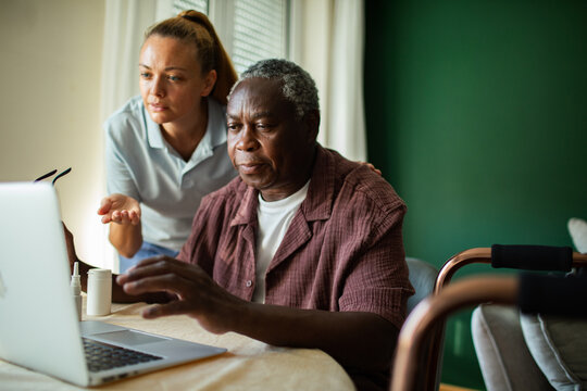Caregiver assisting senior man using laptop at home