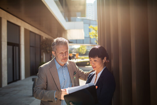 Two business colleagues reviewing documents outside office building