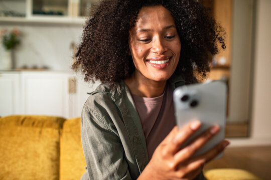 Smiling woman using smartphone at home on couch