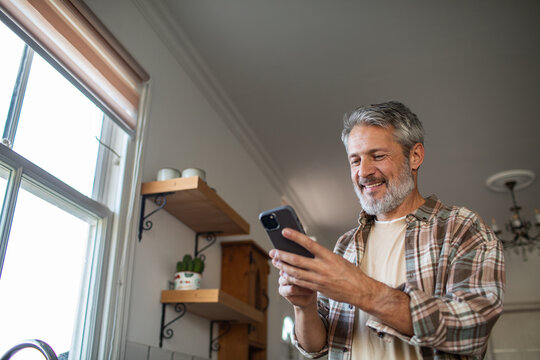 Smiling middle-aged man using smartphone in home kitchen