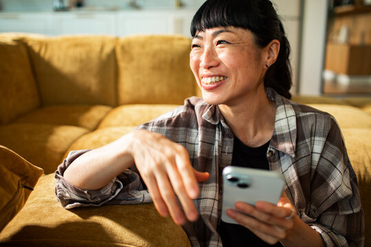 Smiling woman using smartphone on living room sofa