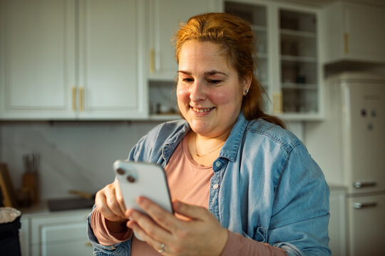 Smiling woman using smartphone in home kitchen