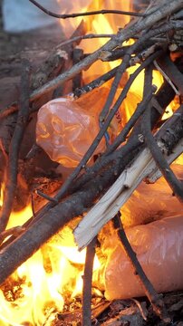 Detrimental practice of burning plastic bottles and household waste in a campfire, a dangerous action that releases toxic chemicals and harmful dioxins, contributing to air pollution