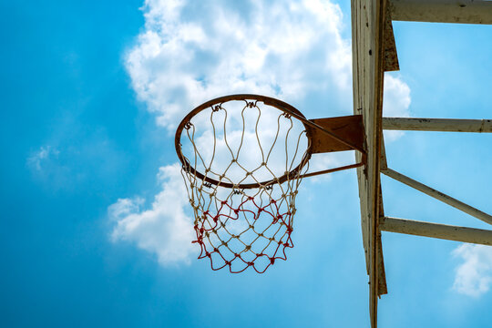 Outdoor basketball hoop and net shot from low angle against bright blue sky.