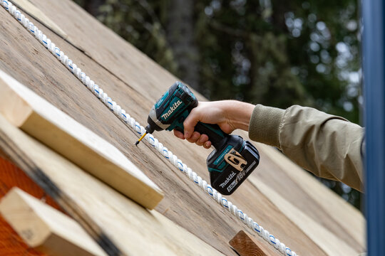 La Tuque, Quebec, 11 May 2026 : A person's hand operates a Makita impact driver, screwing into a wooden surface with a safety rope.