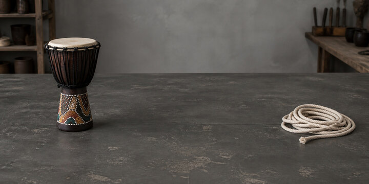 Painted djembe drum and coiled cotton rope on matte worktable, craft preparation and creativity concept