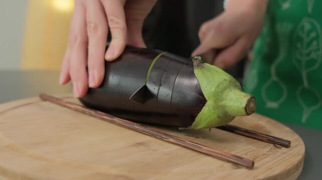 A person in a green apron slices a dark leaf-wrapped item on a wooden board with chopsticks nearby, in a Cooking kitchen setting.