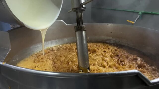 Caramel sauce being continuously mixed in an industrial steam-heated kettle during food manufacturing operations. Large-scale cooking process supporting product consistency, texture control, and comme