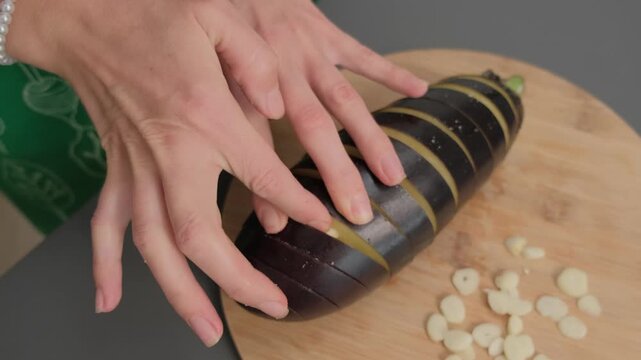 Adult female hands apply light paste to dark striped cylinder on wooden board, with pearl bracelets, in Cooking location during daytime.