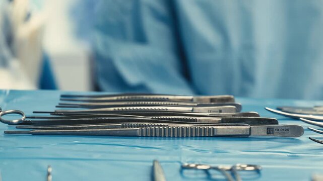 Sterile surgical instruments arranged on a blue operating table before surgery. Prepared set of metal clamps, forceps, tweezers and instrument holders in an operating room.
