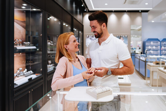 Smiling partners examining diamond rings and accessories across a polished display counter during a shopping trip in a high-end boutique.