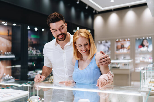 Excited man and woman browsing and selecting expensive diamond rings and accessories together inside a modern commercial boutique.