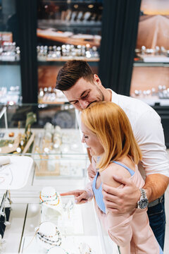 Excited man and woman browsing and selecting expensive diamond rings and accessories together inside a modern commercial boutique.