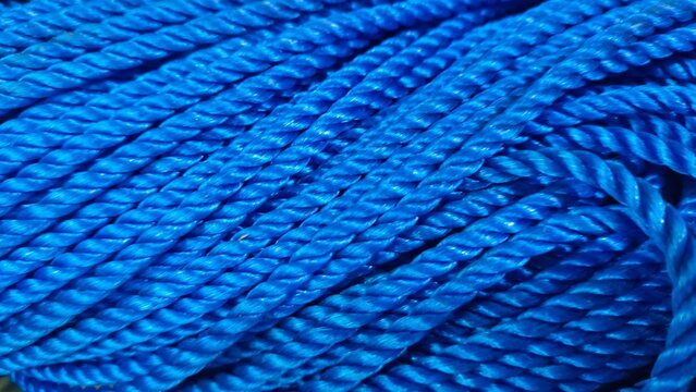Close up of bright blue nylon rope coiled together. The detailed twisted texture of the rope creates a pattern. Concept of rope, nylon, blue, texture, pattern, background, nautical, marine, fishing, i