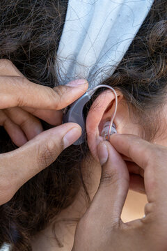 Hands adjusting a modern hearing aid behind and into a person's ear, assisting with hearing impairment and communication
