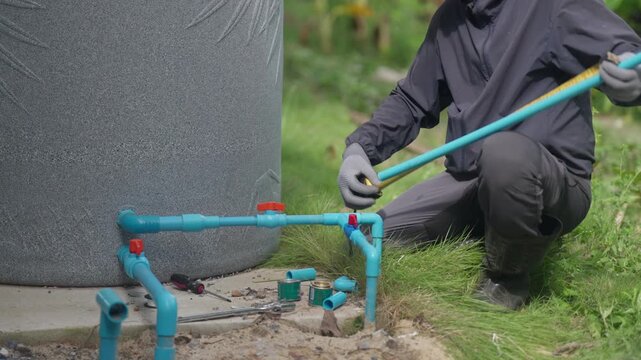 Plumber repairs residential water supply pipes and valves outdoors, representing home maintenance, plumbing service, pipe installation, water system inspection, and household repair.