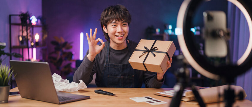 Content creator live streaming unboxing gift box with ring light and laptop in cozy neon home studio for ecommerce, digital marketing, and social media video production