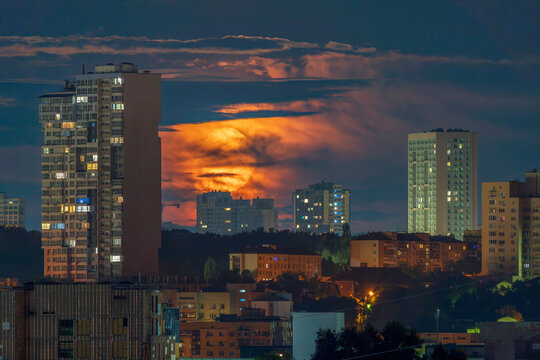 Massive orange full moon setting behind illuminated city skyscrapers at night