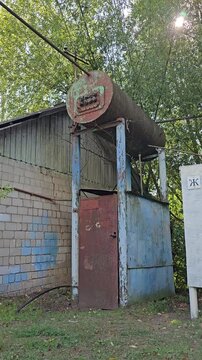 Old industrial hot water tank mounted above a small utility building showing vintage engineering and weathered metal equipment