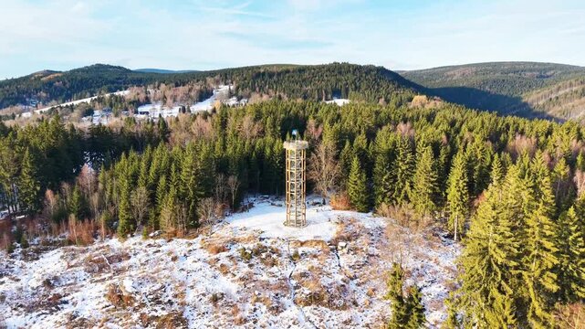 Aerial view of the wooden lookout tower at Svetly vrch surrounded by a snow-covered pine forest in Albrechtice v Jizerskych horach, Liberecky kraj, Czechia.