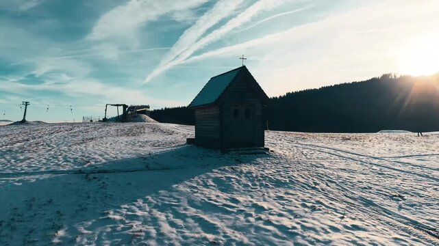 Aerial view of Wooden Chapel in Marianska Hora surrounded by snow-covered fields and distant hills in Albrechtice v Jizerskych horach, Liberecky kraj, Czechia.