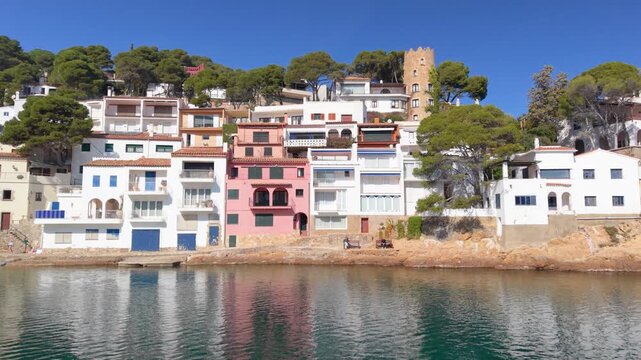 Aerial view of colorful houses nestled along the rocky coastline surrounded by pine trees and the Mediterranean Sea in Begur, Catalunya, Spain.