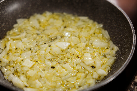 Diced onions sauteing in olive oil in frying pan closeup.