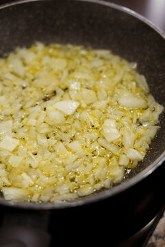 Diced onions sauteing in olive oil in frying pan closeup.