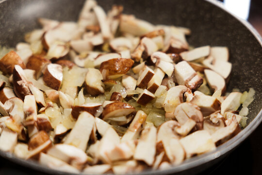 Sliced mushrooms and onions sauteing in frying pan on stove.