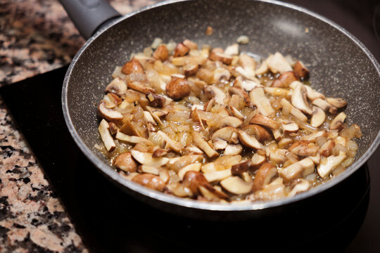 Sliced mushrooms and onions sauteing in frying pan on stove.