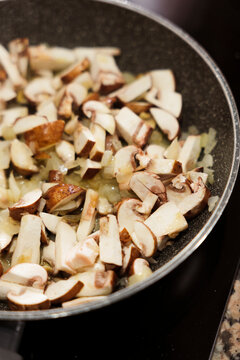 Sliced mushrooms and onions sauteing in frying pan on stove.