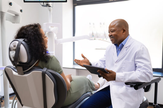 Black male dentist discussing treatment options with smiling female patient using a digital tablet in a modern dental clinic, emphasizing communication and personalized oral care