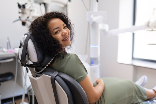 Relaxed black female patient smiling in a dental chair before examination, highlighting a comfortable experience in a clean modern dentistry clinic with professional care
