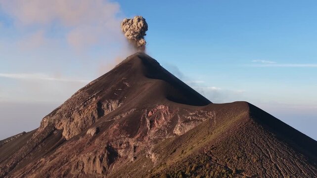 Aerial view of Volcan de Fuego erupting with a plume of ash rising into the clear blue sky above the rugged volcanic slopes in Yepocapa, Chimaltenango Department, Guatemala.