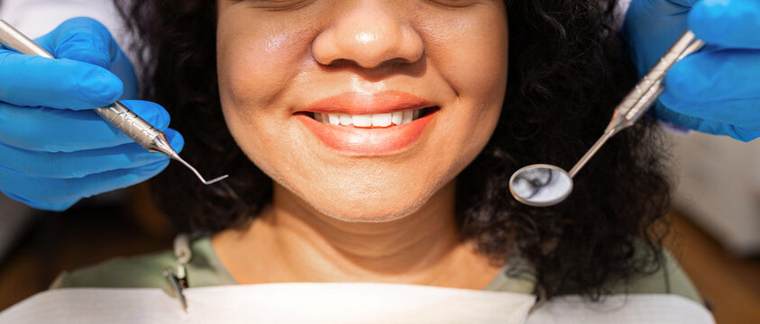 Closeup portrait of smiling female patient during dental examination with professional instruments, emphasizing healthy teeth, preventive care and quality dentistry services