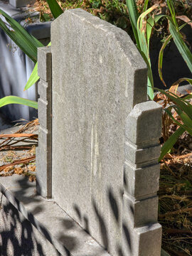 Weathered stone grave marker in cemetery garden with green leaves and sunlight shadows