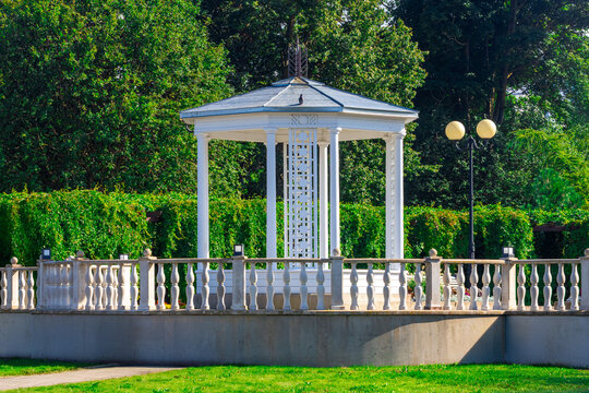 White gazebo pavilion with columns stone balustrade park greenery sunny day