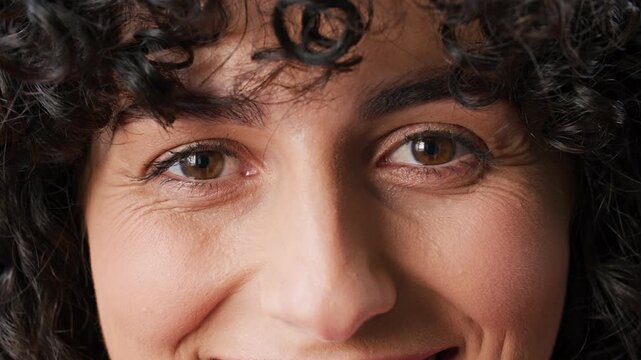 Close up of smiling young woman with curly dark hair and expressive brown eyes. Happy Caucasian female looking at camera. Natural beauty portrait with genuine emotion and soft daylight.