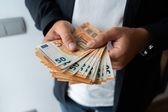 Close-up of a person holding and counting a large stack of fifty euro banknotes indoors, representing income, savings, salary, wealth and personal financial management.